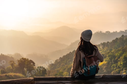 Preview: Happy young woman traveler relaxing and looking at the beautiful sunrise on the top of mountain