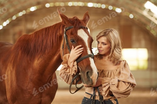 Preview: Standing and embracing the animal. Beautiful young woman is with horse indoors