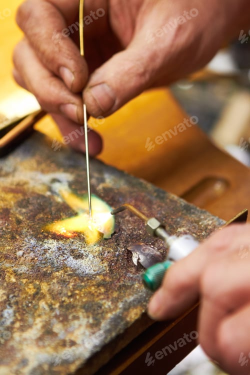 Preview: Cropped view of a manufacturing jeweler heating up solder and using a soldering pick