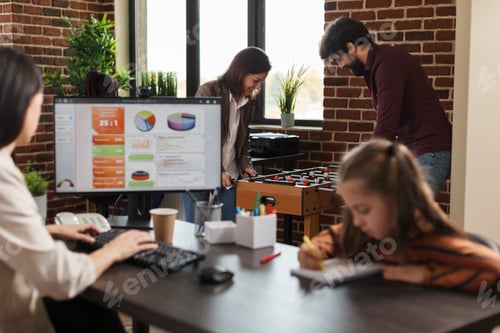 Preview: Agency business people playing table soccer while young woman working sitting at computer.