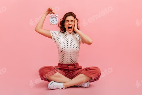 Preview: Brunette girl screaming with closed eyes. Stressed woman holding clock on pink background.