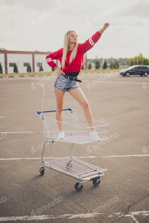 Preview: Confident young hipster riding shopping trolley