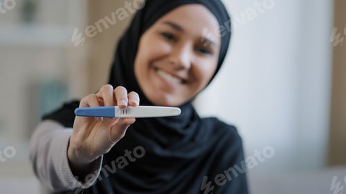 Preview: Joyful islamic young woman in hijab smiling happily holding pregnancy test excited pregnant lady