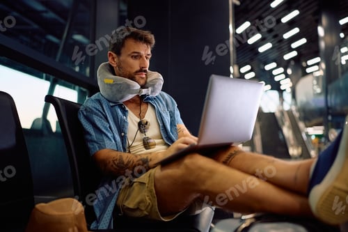 Preview: Male tourist using laptop while waiting at airport terminal.