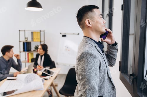Preview: Asian business man talking on mobile phone in modern loft office