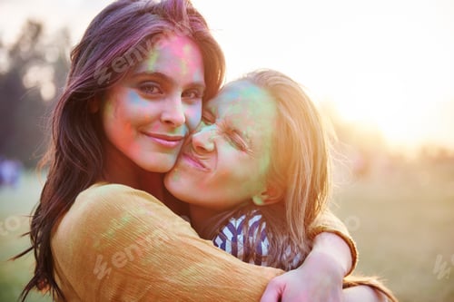 Preview: Two young women with faces covered in coloured chalk powder hugging at Holi Festival, portrait