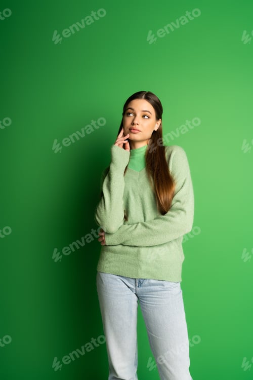 Preview: Pensive teen girl in jumper and jeans looking away on green background