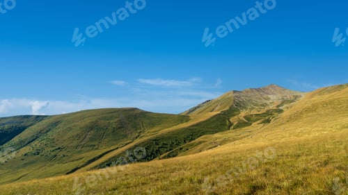 Preview: Wide open mountain landscape with grassy hills and a bright blue sky.