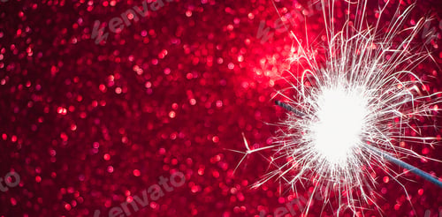 Preview: New Year celebration. Sparkler on red background. Christmas night. Bright sparks of fire and bokeh.