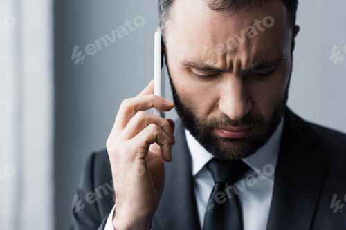 Preview: serious bearded man in black suit looking down while using smartphone