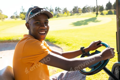 Preview: Portrait of happy african american young man wearing cap driving golf cart at golf course