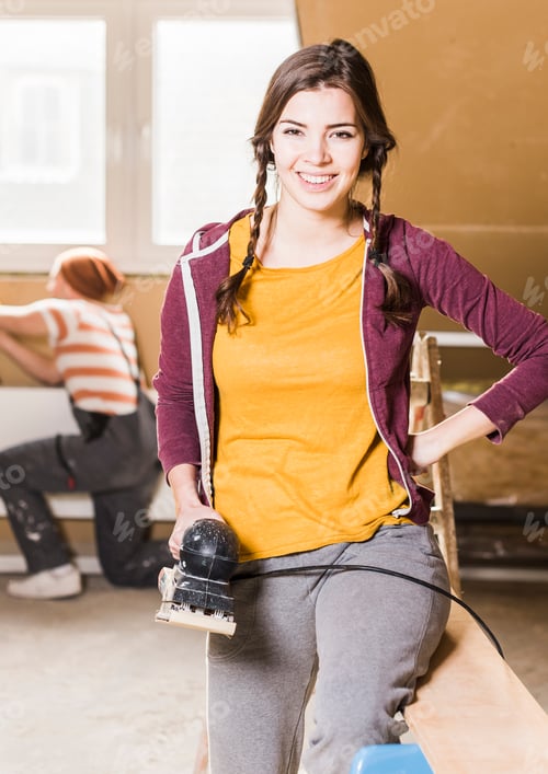 Preview: Young woman sanding planks on construction site of her new home