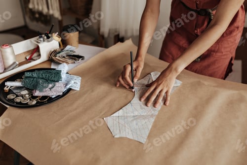 Preview: Tanned woman in linen red dress draws cloth pattern on craft paper. Fashion designer creates garmen