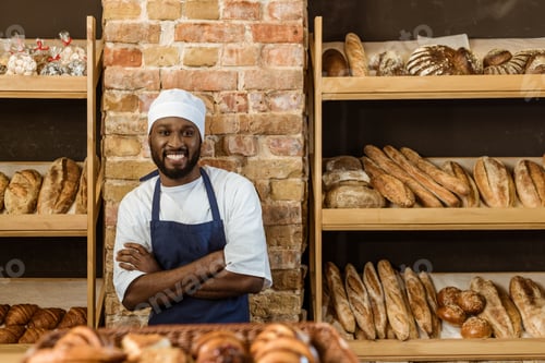 Preview: handsome smiling baker with folded arms standing at pastry store
