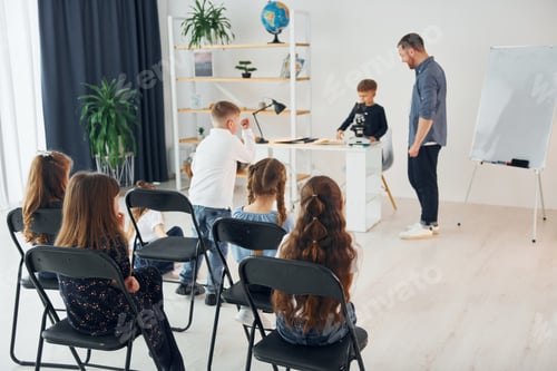 Preview: Looking at the boy with microscope that is on the table. Group of children students in class