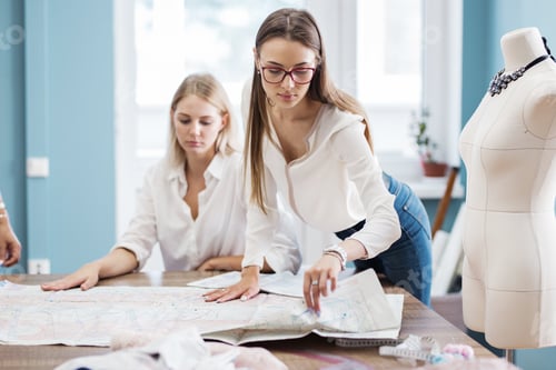 Preview: Two smart-looking pretty women wearing white shirts are pointing at the sewing cutting-out. Fashion