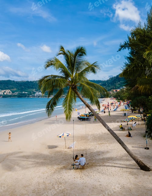Preview: A couple of men and women on a swing under a palm tree at the beach of Patong Phuket Thailand