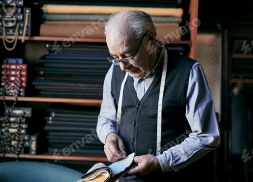 Preview: Tailor with measuring tape around his neck inspecting fabric samples.