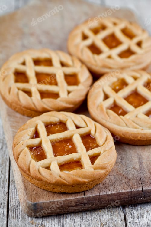 Preview: Fresh baked tarts with marmalade or apricot jam filling on cutting board on on rustic wooden table.