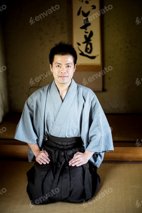 Preview: Japanese man wearing kimono sitting on floor in traditional Japanese house, looking at camera.