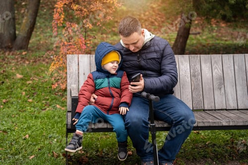 Preview: Beautiful 35 year old caucasian father with toddler 4 year son sits on a bench in a city park