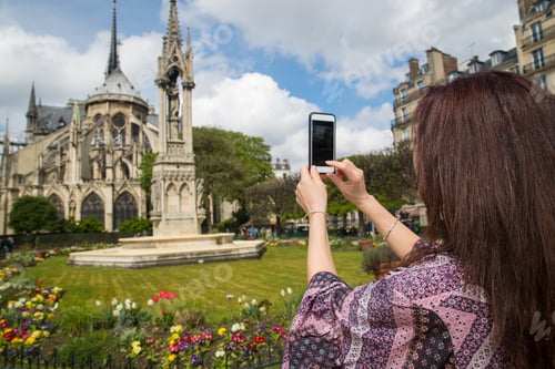 Preview: Woman taking photo with cell phone at Notre-Dame in Paris, France