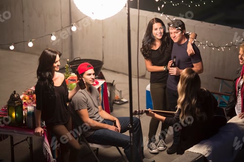 Preview: Young adult friends listening to guitar at rooftop party