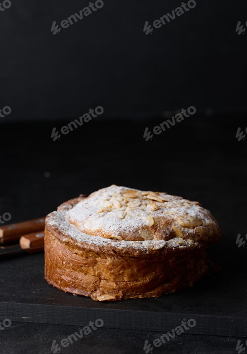Preview: Round pastry with almonds and butter sprinkled with powdered sugar on the table, puff pastry