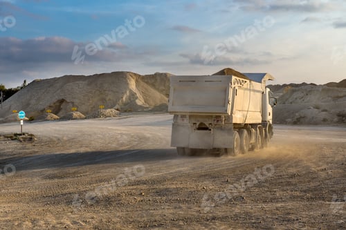 Preview: a white truck on a road on the background of piles of stone in a quarry, evening sky