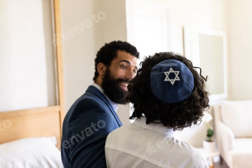 Preview: Jewish man wearing kippah smiling and talking with friend at home