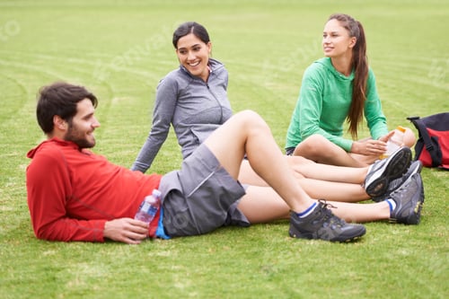 Preview: Fitness down time. Shot of a group of young people relaxing on the grass after exercising.