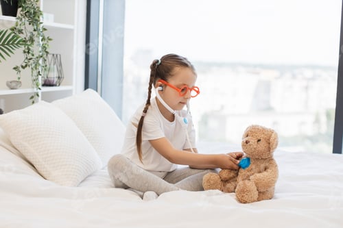 Preview: Girl with toy doctor kit examining teddy on bed in own room