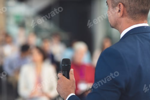 Preview: Rear view of mixed race businessman speaking at a business seminar in modern office