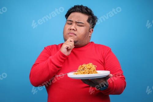 Preview: Studio Shot Of Young Fat Man Gesture Thinking Before Eat Fried Noodle Over Blue Background