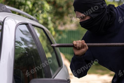 Preview: masked thief standing near the car and trying to smash the window with cowbar