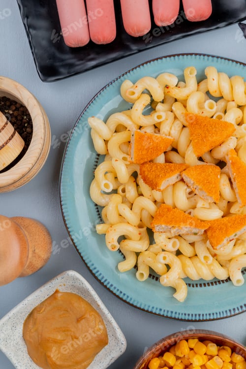 Preview: top view of pasta on a blue plate with fried chicken pieces with sausages on a black plate
