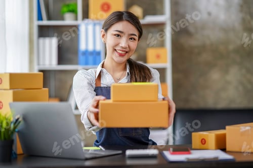 Preview: Attractive Asian businesswoman handing a box to the camera Young Asian small business owners use com