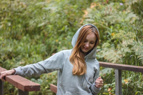 Preview: Girl traveler with red long hair standing on forest bridge and looking at wild nature