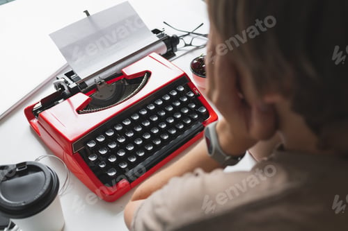 Preview: Woman writer thoughtfully working on a book on her Desk red typewriter