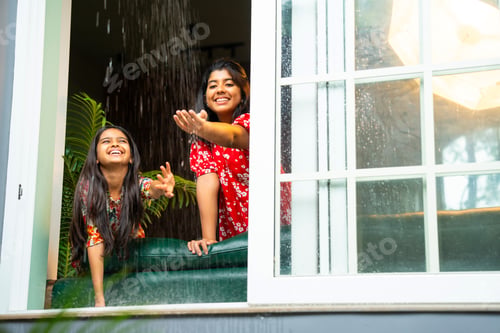 Preview: Two Indian girls happily enjoy monsoon rain while touching water drops from open home window
