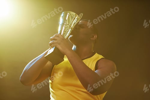 Preview: Black Male Sportsman Kissing Trophy and Celebrating Victory
