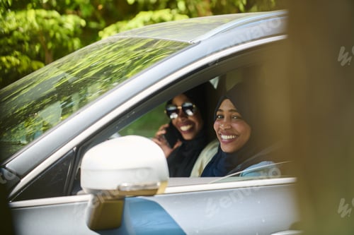 Preview: Two Muslim women wearing hijab converse on a smartphone while traveling together in a car through