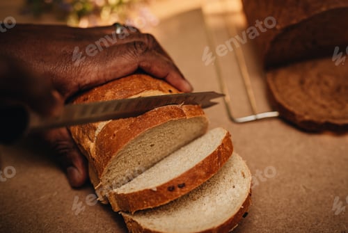 Preview: Close up of African American or black man cutting a slide of freshly baked bread