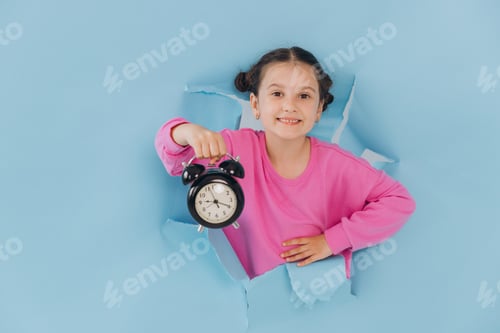 Preview: Little girl looking out of a torn hole in a blue paper and showing a clock, discount time