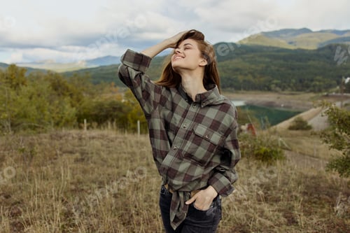 Preview: A woman in a plaid shirt enjoying the scenic view of mountains in a peaceful field landscape