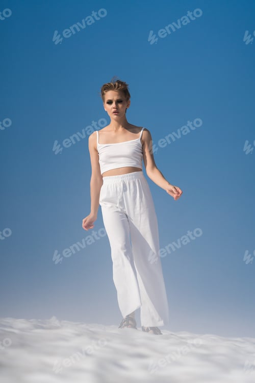 Preview: Fashionable blond woman walks through snow with light fog on sunny weather with blue sky