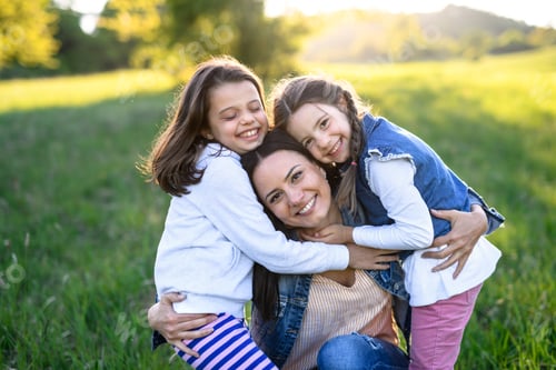 Preview: Mother with two small daughters having fun outdoors in spring nature, hugging