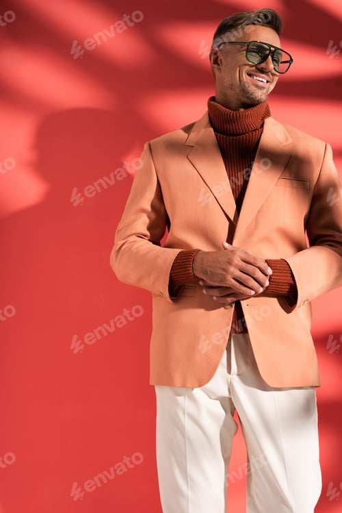 Preview: fashionable man in sunglasses and blazer standing on red with shadows