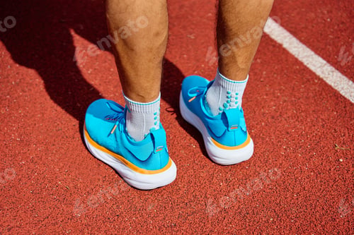 Preview: Athlete Wearing Bright Blue Running Shoes on Red Stadium Track During Training