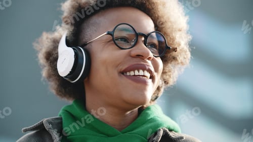 Preview: African american happy woman wearing headphones while walking outdoors